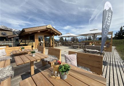 Eine gemütliche Terrasse mit Holzmöbeln und Blick auf die Berge. Ein Hinweis zeigt auf die Bar des Restaurants.