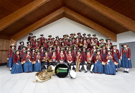 Eine große Gruppe von Musikern in traditioneller Tracht steht in einem Raum. Sie halten Instrumente und lächeln in die Kamera.