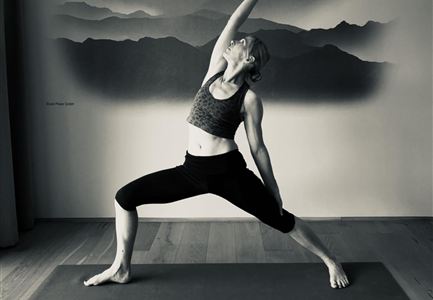 A woman is practicing yoga in an elegant pose on a yoga mat. In the background, a minimalist mountain landscape is visible.
