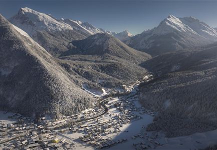Un paesaggio alpino pittoresco con montagne coperte di neve e un piccolo villaggio nella valle. Il cielo è sereno e la luce si diffonde sulla scena invernale.