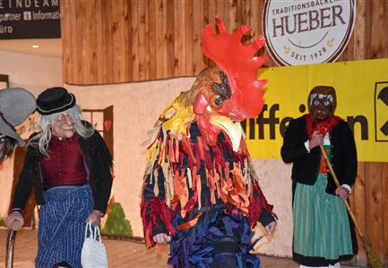 Eine bunte Aufführung mit verkleideten Personen, die Masken tragen. Die Figuren scheinen Teil eines traditionellen Festes oder Brauchs zu sein.