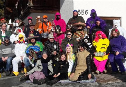 A group of people in colorful costumes gathers in front of a house. They laugh and happily pose for the photo.