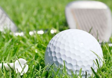 Ein weißer Golfball liegt auf grünem Gras, umgeben von Golftee und Golfschlägern. Die Szene zeigt eine entspannte Golfumgebung.