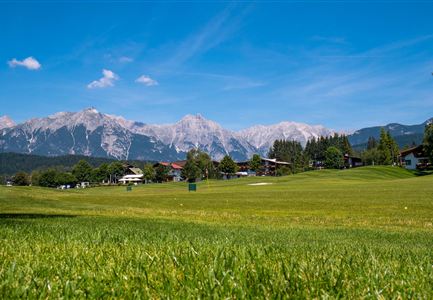 Eine grüne Wiese mit einem klaren blauen Himmel und majestätischen Bergen im Hintergrund. Die Szenerie ist ruhig und einladend.