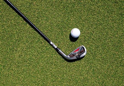 Ein Golfschläger liegt auf grünem Rasen neben einem Golfball. Die Szene zeigt eine typische Golfsituation.
