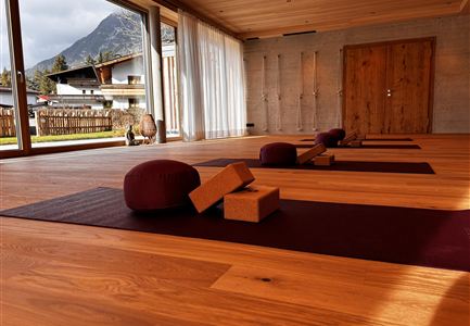 A quiet room with wooden floors and large windows.
In the foreground, there are yoga cushions and blocks, while the mountains are visible in the background.