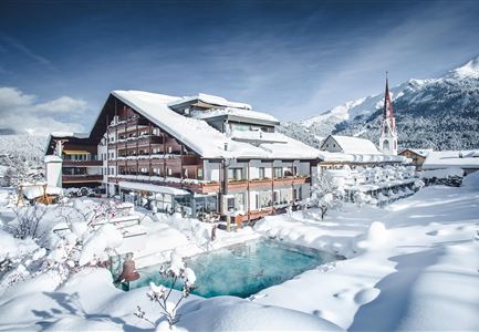 A snow-covered hotel in a winter landscape. In the background, mountains and a church can be seen.