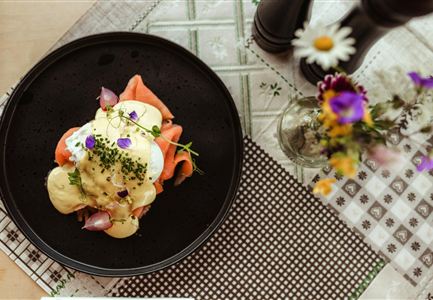 Een elegant gerecht met zalm, gepocheerde eieren en een romige saus. Het eten is liefdevol gegarneerd met verse kruiden en eetbare bloemen.