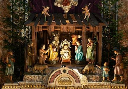 A traditional Christmas nativity scene with figures representing the birth of Jesus. Surrounded by fir trees and a wooden frame.
