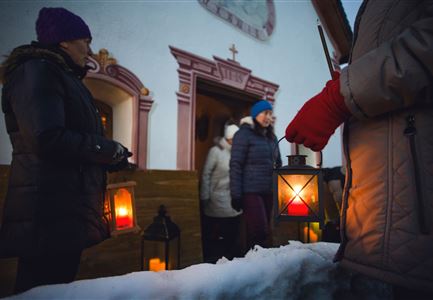 Un gruppo di persone tiene lanterne e sta davanti a un edificio nella neve. L'atmosfera è festosa e invernale.