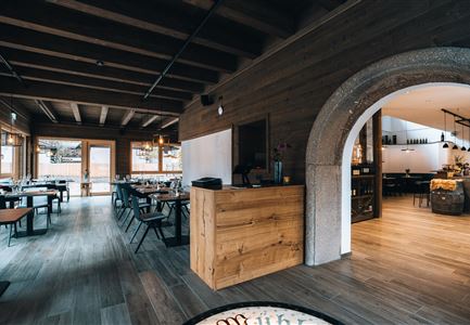 Ein modernes Restaurant mit Holzdekor und großen Fenstern. Der Empfangsbereich und der Essbereich sind freundlich und einladend gestaltet.