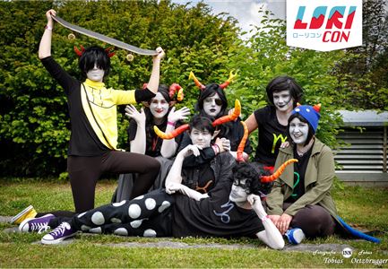 Eine Gruppe von Cosplayern in bunten Kostümen zeigt kreative Charaktere mit farbenfrohen Hörnern. Sie posieren fröhlich im Freien, umgeben von grüner Vegetation.