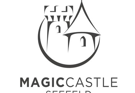 Ein stilisiertes Logo eines Schlosses mit einem Turm und einem Zelt. Der Text „Magic Castle Seefeld“ steht darunter.