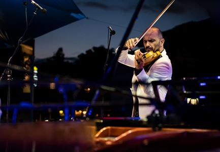 Ein Musiker spielt Violine auf einer Bühne bei Nacht. Die Umgebung ist beleuchtet und schafft eine stimmungsvolle Atmosphäre.