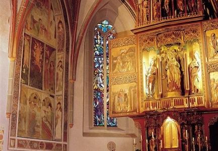 Ein schöner Innenraum einer Kirche mit detaillierten Wandmalereien und einem kunstvollen Altar. Das farbenfrohe Fenster lässt Licht in den Raum strömen.