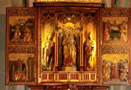 Ein kunstvoller Altar mit Reliefs und goldenen Verzierungen. Umgeben von bunten Fenstern, die Licht ins Innere bringen.