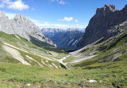 Un'impressionante paesaggio montano con alte vette e prati verdi. Il cielo limpido e le montagne circostanti donano alla scena un'atmosfera maestosa.