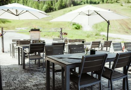 Ein ruhiger Außenbereich mit Tischen und Stühlen. Sonnenschirme bieten Schatten in einer grünen Umgebung.