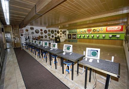 Ein Schießstand mit mehreren computergestützten Schießständen und Tischen. An den Wänden hängen zahlreiche Medaillen und Abzeichen.