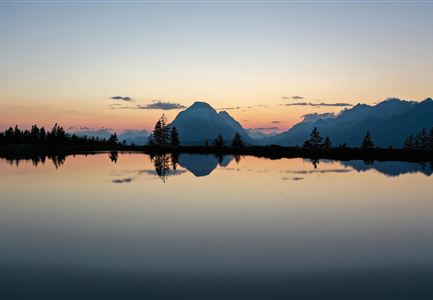 Eine ruhige Berglandschaft bei Sonnenuntergang, reflektiert im Wasser. Die Farben des Himmels sind sanft und harmonisch.