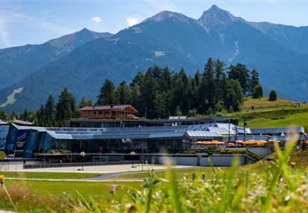 Eine moderne Anlage unterhalb majestätischer Berge. Die Umgebung ist grün und sonnig, ideal für Outdoor-Aktivitäten.