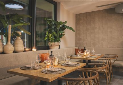 Ein modernes Restaurant mit eleganten Holztischen und stilvollen Stühlen. Die gemütliche Atmosphäre wird durch Pflanzen und sanftes Licht unterstrichen.