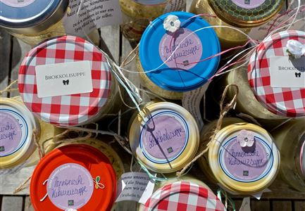 Bunte Gläser mit verschiedenen Aufstrichen und Etiketten. Die Gläser sind kreativ verpackt und stehen auf einer Holzoberfläche.