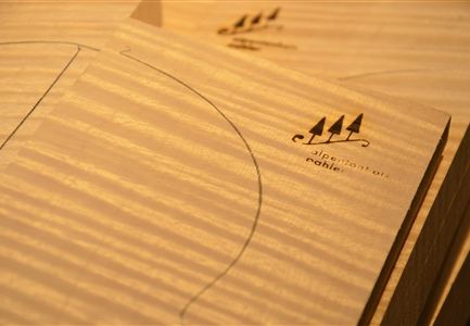 Eine helle Holzoberfläche mit eingezeichneten Linien und einem Logo. Die Struktur des Holzes ist gut sichtbar und verleiht dem Bild eine natürliche Ausstrahlung.