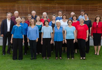 Een groep mensen staat op een weide voor een houten wand. Ze dragen verschillende tops in verschillende kleuren en lachen vriendelijk naar de camera.