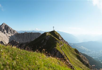 Eine beeindruckende Berglandschaft mit grünen Wiesen und hohen Gipfeln. Im Hintergrund ist ein klarer Himmel zu sehen.