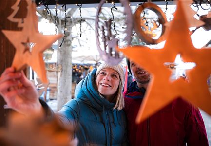 Ein Paar betrachtet Weihnachtsdekorationen in Form von Sternen. Die Umgebung ist festlich und winterlich gestaltet.