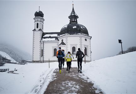 A group of runners is heading towards a beautiful, wintery church. The ground is covered in snow and the surroundings are misty.
