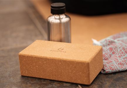 Eine elegante Korkbox steht neben einer silbernen Wasserflasche und einem bunten Tuch. Die Anordnung vermittelt einen natürlichen, minimalistischen Look.
