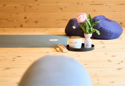 Ein ruhiger Raum mit Holzfußboden und sanften Farben. Auf der Matte stehen ein Kerzenhalter, eine Blume und eine Tasse.