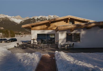 Ein modernes Gebäude inmitten von Schnee mit Blick auf Berge. Draußen stehen Tische und Stühle für Gäste.
