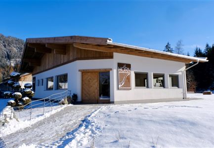 Ein modernes Gebäude im Schnee mit einem Holzdach und großen Fenstern. Umgeben von einer wunderschönen winterlichen Landschaft.
