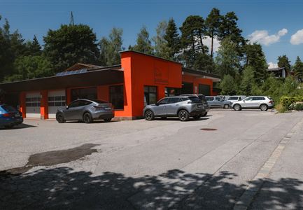 Ein modernes Gebäude mit leuchtend orangefarbenem Anstrich. Vor dem Gebäude parken mehrere Autos auf einem gut beleuchteten Platz.