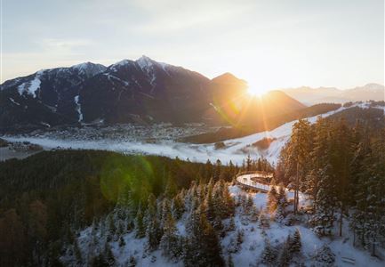 Eine beeindruckende Winterlandschaft mit schneebedeckten Bergen und einer tiefen, klaren Aussicht. Die Sonne geht hinter den Bergen auf und taucht die Szene in warmes Licht.