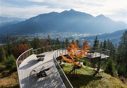 Eine Aussichtsplattform aus Holz mit Blick auf die Berge und das Tal. Bunte Bäume und eine klare Himmelssicht sorgen für eine wunderschöne Landschaft.