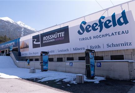 <p>Ein großes Werbeschild für Seefeld und Rosshütte in Tirol. Im Vordergrund stehen zwei E-Ladestaionen neben einer schneebedeckten Fläche.</p>