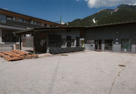 Ein modernes Gebäude mit Solarpanelen auf dem Dach. Im Vordergrund liegen Holzpaletten auf dem grauen Boden.