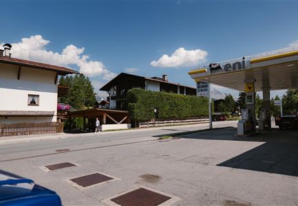 A street with a view of two traditional buildings and a gas station. The sky is blue with some white clouds.