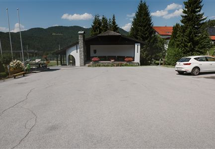 Ein ruhiger Parkplatz vor einem modernen Gebäude umgeben von Bäumen und Bergen. Der Himmel ist klar und blau.