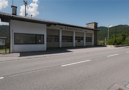 A modern fire station with large windows. In the background, green hills and a blue sky can be seen.