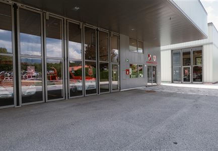 Eine moderne Gebäudeansicht mit großen Glasfenstern und einem klaren Himmel. Der Eingangsbereich ist gut beleuchtet und einladend.