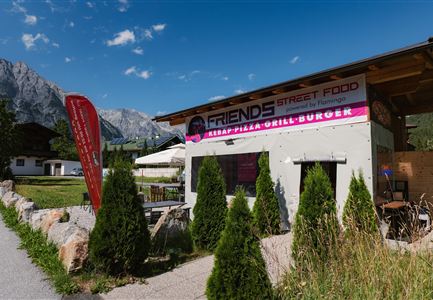 A small snack bar called "Friends Street Food." It offers kebab, pizza, grill, and burgers, surrounded by beautiful scenery and mountains.