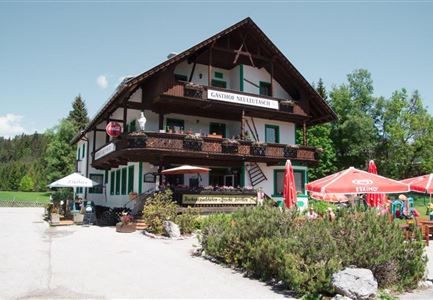 Ein traditionelles Gasthaus im bayerischen Stil mit einem schönen Balkon. Umgeben von grünen Bäumen und sonnigem Wetter.