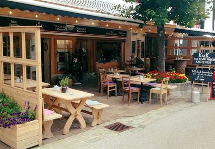 Ein gemütliches Restaurant mit Holzterrasse und bunten Blumen. Die Tische sind einladend und das Ambiente ist freundlich.