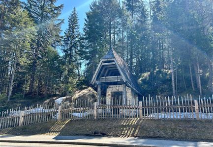 Eine malerische Landschaft mit einem traditionellen Holzgebäude und vielen Bäumen. Der Bereich ist ruhig und von einem Holzzaun umgeben.