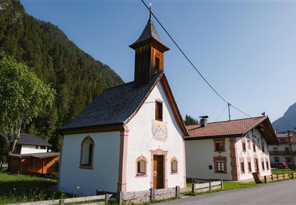 A charming building with a bell tower, surrounded by mountains. The architecture is traditional and colorful, ideal for a rural setting.